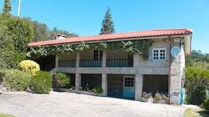 A two-story stone building with a red-tiled roof, a covered porch, and a blue door. - Casas de Pindela (Vila Nova de Famalicao)
