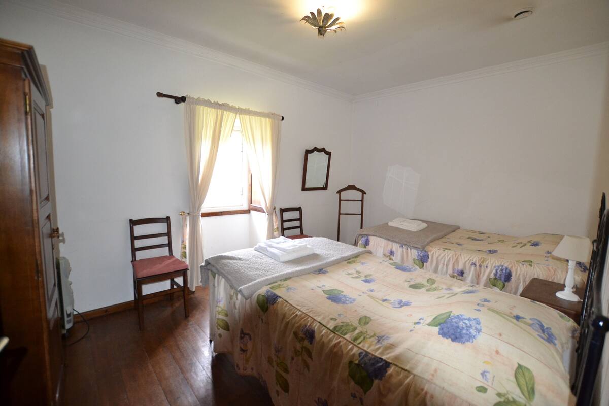 Une chambre avec deux lits, une chaise, une petite table, un miroir et une fenêtre avec des rideaux.