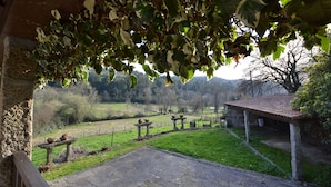 A stone bench with a rustic shelter, a stone pathway, and a view of a green landscape with trees and a distant building. - Casas de Pindela (Vila Nova de Famalicao)