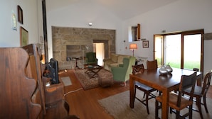 A spacious living room with a stone fireplace, a dining table with chairs, a green armchair, and a wooden coffee table. - Casas de Pindela (Vila Nova de Famalicao)