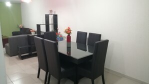 A dining area with a black table and chairs, a small side table with a vase of flowers, and a green wall in the background. - House in private subdivision (Aguascalientes)