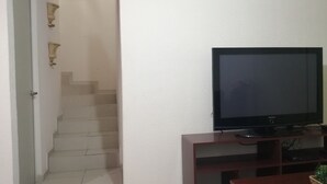 A living room with a flat-screen TV on a wooden stand, a staircase leading to another room, and a door with a handle. - House in private subdivision (Aguascalientes)
