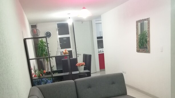 A modern living room with a grey sectional sofa, a small table, and a mirror on the wall. - House in private subdivision (Aguascalientes)
