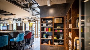 A modern bar area with bar stools, shelves with bottles, and a seating area with a view of the outdoors. - MASEVEN München Messe Trudering (Munich)