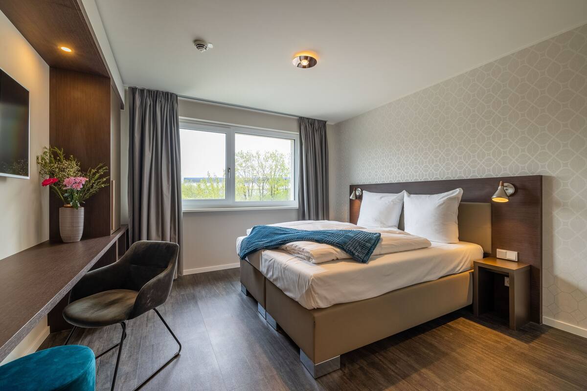 Une chambre d’hôtel moderne avec un grand lit, un bureau et une fenêtre avec des rideaux.