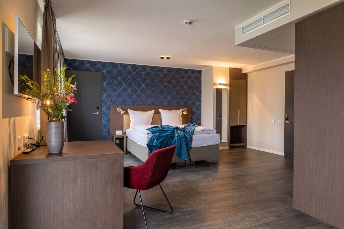 Une chambre d’hôtel moderne équipée d’un lit, d’un bureau, d’une chaise et d’un vase de fleurs.
