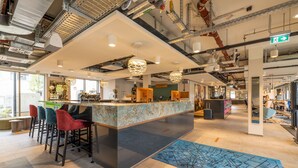 A modern bar area with a marble counter, multiple bar stools, and pendant lighting. - MASEVEN München Messe Trudering (Munich)