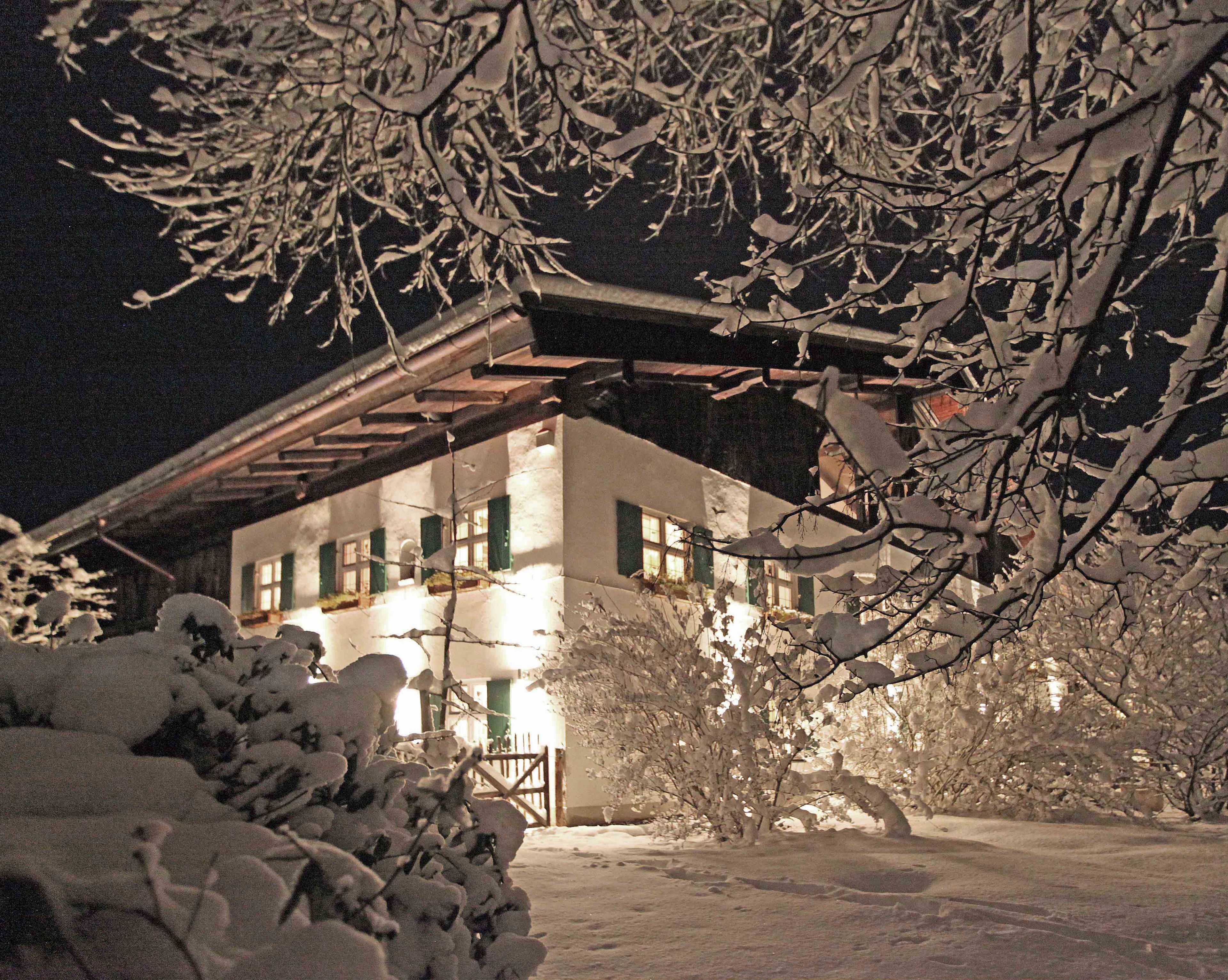 Ein mit Schnee bedecktes Gebäude mit einer Holzfassade und grünen Fensterläden, umgeben von schneebedeckten Bäumen und einem klaren Nachthimmel.