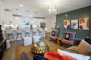 A modern living room with a sofa, coffee table, and chairs, a kitchen in the background, and artwork on the wall. - 🥳​🎉  Music City Bachelor/Bachelorette Party Pad- Close to Downtown! (Nashville)