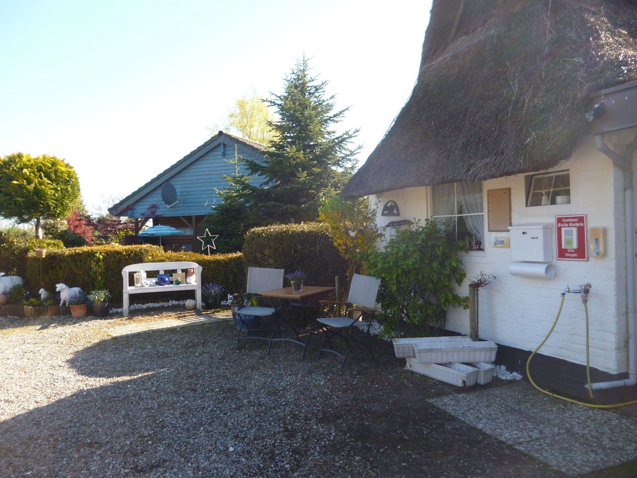 A rustic building with a thatched roof, a small outdoor seating area with a bench and table, and a gravel ground.