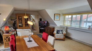 Uma sala de estar aconchegante com uma mesa de jantar de madeira, cadeiras vermelhas, uma poltrona estampada e uma televisão.