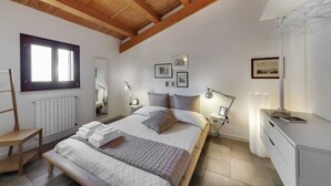 Ein Schlafzimmer mit Holzbalkendecke, einem großen Bett mit Kissen und Decke, einem Nachttisch mit Lampe und einer Kommode.