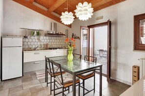Cozinha moderna com armários brancos, mesa de jantar de vidro e duas luminárias pendentes.