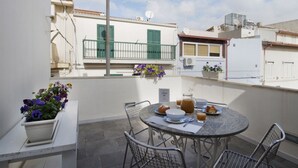 Ein Balkon mit rundem Tisch, Stühlen, einem Blumentopf und einem kleinen Garten.