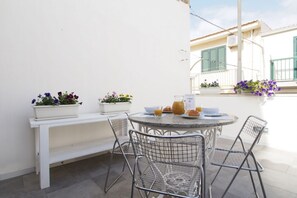 A round table with four metal chairs, a white bench, and two flower pots with flowers. - La Mancina is just 150 meters away from the main beaches of Marina di Ragusa (Marina di Ragusa)