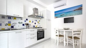 A modern kitchen with white cabinets, a tiled backsplash, a stove, and a dining area with white chairs. - Just 100 meters from one of the most beautiful and renowned beaches of the Ragusa’s coast (Marina di Ragusa)