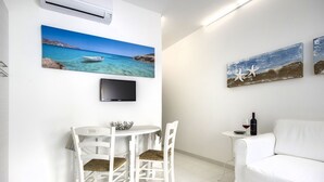 A modern living room with a white sofa, a dining table with two chairs, a flat-screen TV, and artwork on the walls. - Just 100 meters from one of the most beautiful and renowned beaches of the Ragusa’s coast (Marina di Ragusa)