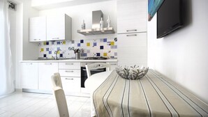 A modern kitchen with white cabinets, a tiled backsplash, and a dining area with a striped tablecloth and a decorative bowl. - Just 100 meters from one of the most beautiful and renowned beaches of the Ragusa’s coast (Marina di Ragusa)