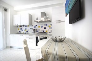 Une cuisine moderne avec des meubles blancs, un pare-feu en carreaux et un coin repas agrémenté d’une nappe à rayures et d’un saladier décoratif.