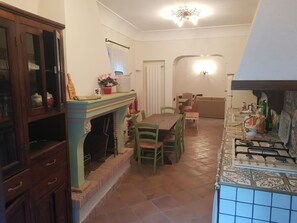 A dining area with a fireplace, green chairs, a wooden cabinet, and a tiled kitchen area with a stove.