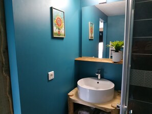 A bathroom with teal walls, a white sink, a mirror, and a framed picture on the wall. - Chambre d'Hotes des Bassins (Saint-Paul-en-Chablais)