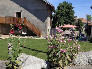 A house with a wooden staircase, a red umbrella, and a garden with flowers. - Chambre d'Hotes des Bassins (Saint-Paul-en-Chablais)