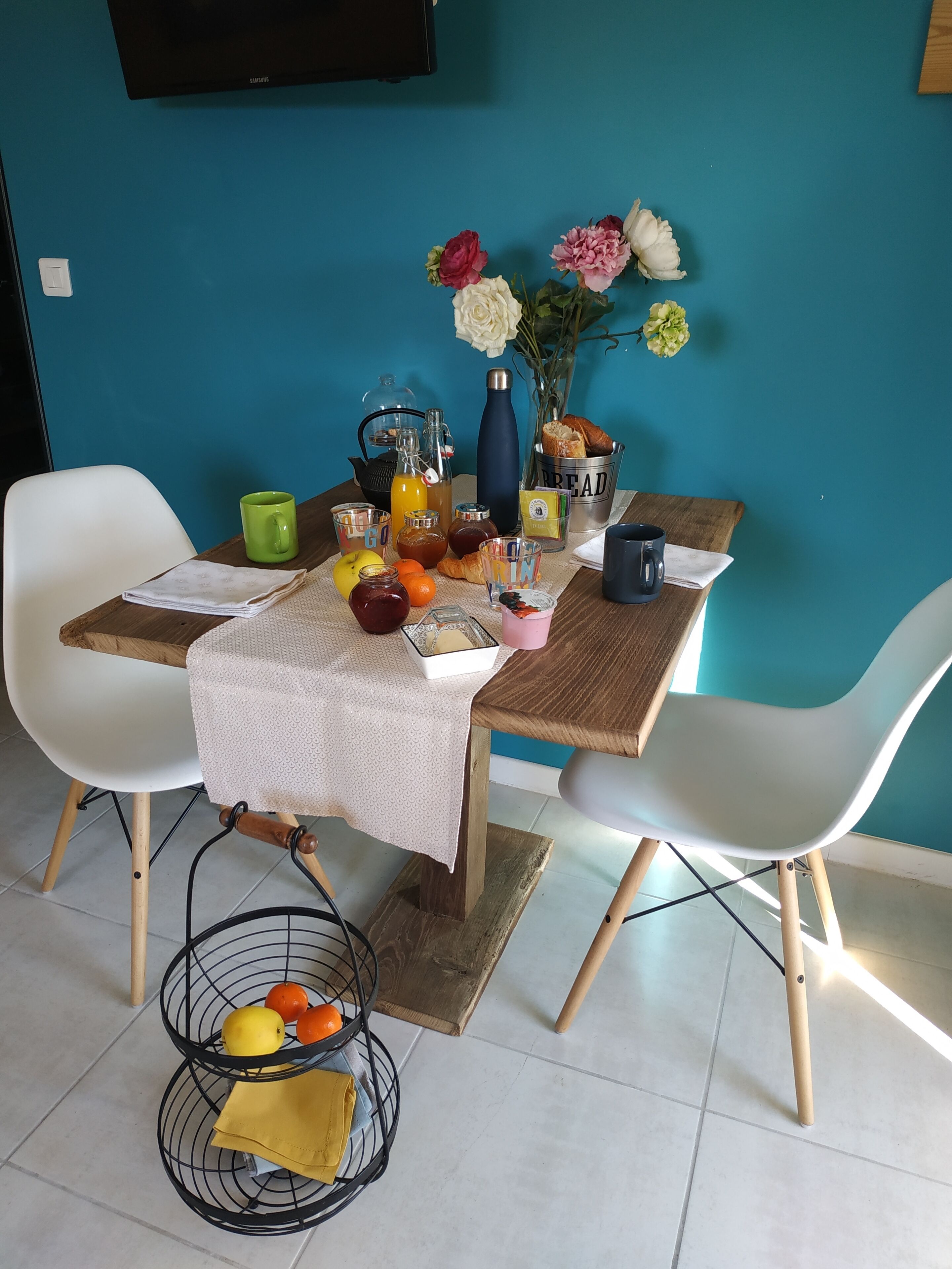 A dining table set with various breakfast items, a vase with flowers, and a fruit basket.