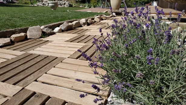 A wooden deck with a stone border, surrounded by a garden with lavender plants. - Chambre d'Hotes des Bassins (Saint-Paul-en-Chablais)