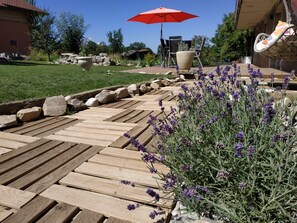 A wooden deck with a stone border, surrounded by a garden with lavender plants. - Chambre d'Hotes des Bassins (Saint-Paul-en-Chablais)