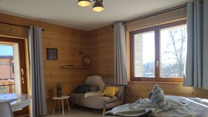 A cozy room with a bed, a chair, a small table, and a window with curtains. - Chambre d'Hotes des Bassins (Saint-Paul-en-Chablais)