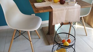 A dining table with a white tablecloth, surrounded by white chairs, with a fruit basket and a vase of flowers on the table. - Chambre d'Hotes des Bassins (Saint-Paul-en-Chablais)