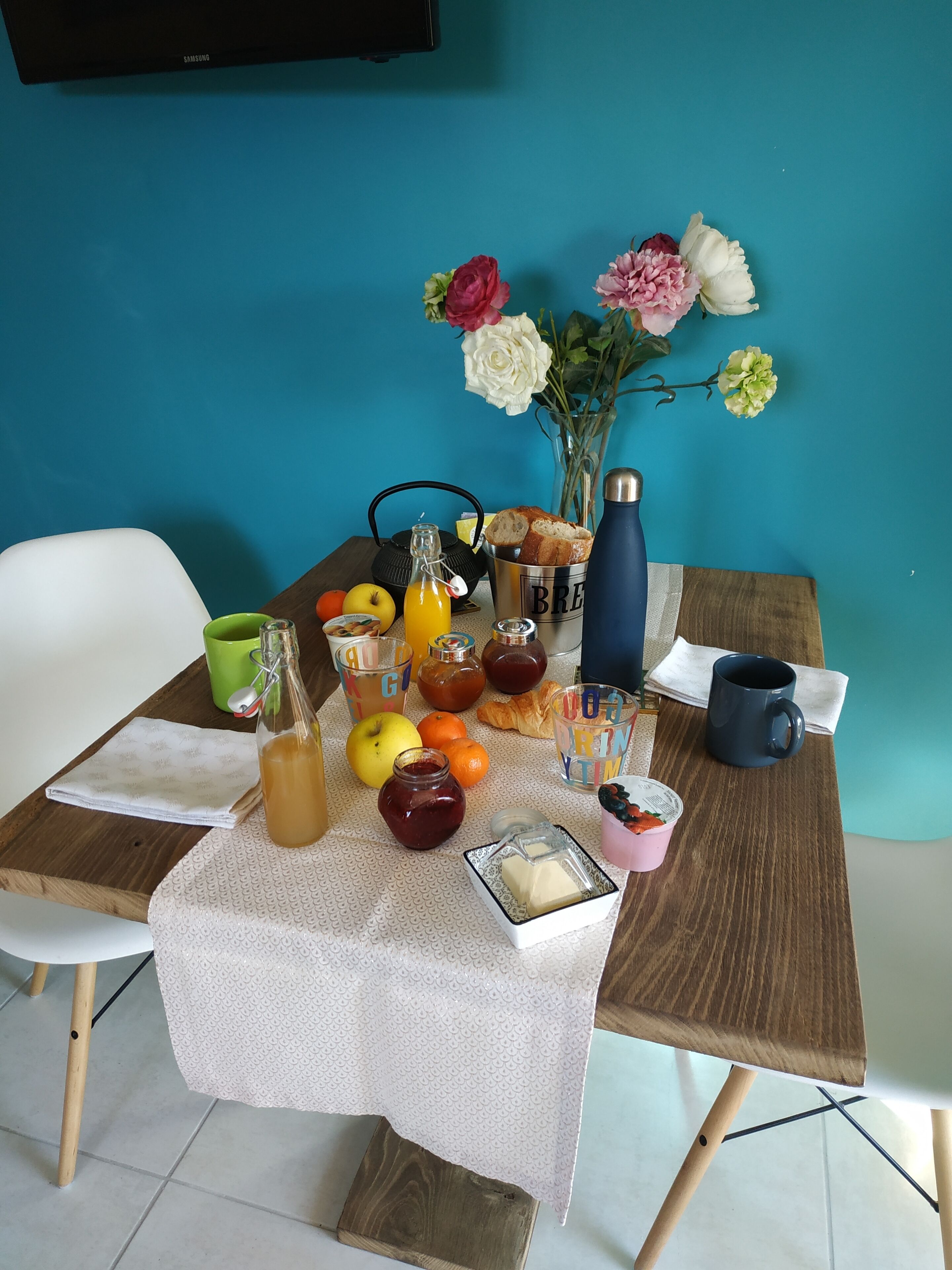 A breakfast table with a variety of food items, a vase with flowers, and a blue water bottle.