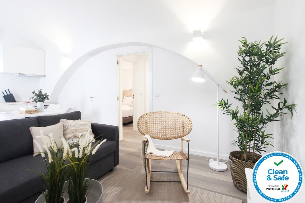 Una sala de estar moderna con un sofá gris, un sillón de mimbre y una planta grande en maceta.