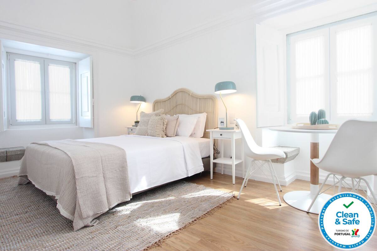 Un dormitorio limpio y moderno con cama, mesitas de noche, un escritorio y sillas.