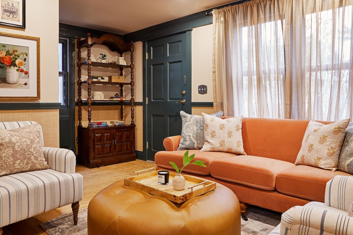 Un salon chaleureux avec des canapés à rayures, une table basse en bois ornée d’un vase et d’une bougie, et une bibliothèque contenant des objets décoratifs.