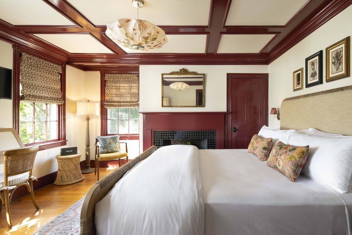 Une chambre à coucher élégamment aménagée, dotée d’un grand lit, d’une cheminée et d’un lustre.