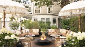 An outdoor seating area with wicker furniture, a central fire feature, and white umbrellas. - Life House, Nantucket (Nantucket)
