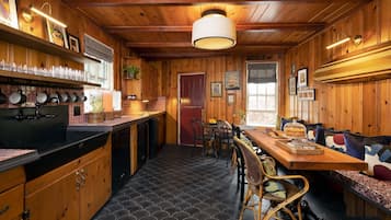 Una cabaña de madera acogedora con cocina, que cuenta con una encimera negra, utensilios colgantes y un comedor con banco y sillas.
