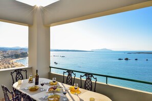 Un balcon avec une table dressée pour le dîner, offrant une vue sur la côte, la mer et la terre au loin.