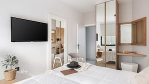 Un dormitorio moderno con cama, televisión montada en la pared, espejo y armario.