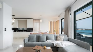 Una sala de estar moderna con un sofá gris, una mesa de centro de madera y vista al mar a través de amplios ventanales.
