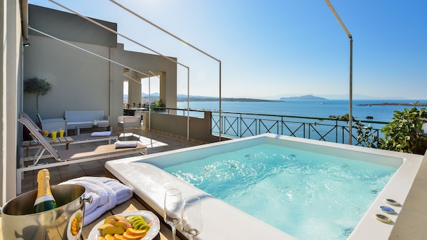Zona de piscina con vista al mar, una silla de descanso, una botella de champán y un plato de fruta.