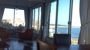 A room with large windows overlooking the sea, furnished with wooden chairs and a table. - Beautiful House Privileged Location Unique View (maldonado)