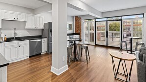Una cocina moderna con armarios blancos, lavavajillas y un comedor con taburetes y una mesa redonda.