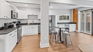Una cocina moderna con armarios blancos, electrodomésticos de acero inoxidable y una isla central con taburetes.