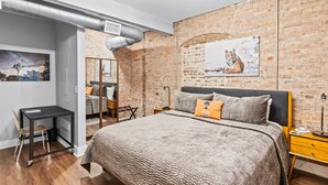 Un dormitorio con una cama grande, un escritorio, una silla, un espejo y una pared de ladrillo.
