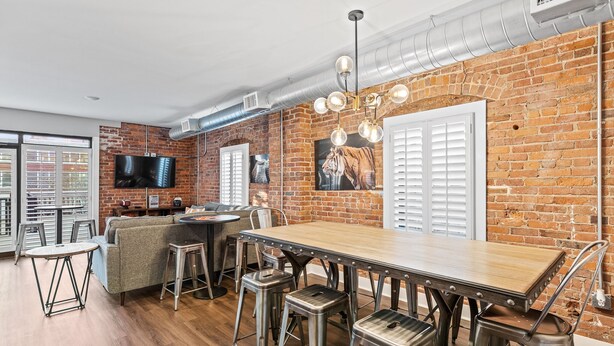 Un comedor con pared de ladrillo, mesa de madera, sillas de metal y una lámpara moderna.