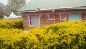 Um edifício com telhado verde e paredes rosa, rodeado por arbustos verdes densos.