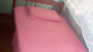 Cama com colcha rosa e cabeceira de madeira.