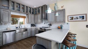 A modern kitchen with grey cabinets, a central island with bar stools, stainless steel appliances, and pendant lighting. - Seascape🐚Bayfront Home🌊Boat Slip🐶Dogs OK (Navarre)